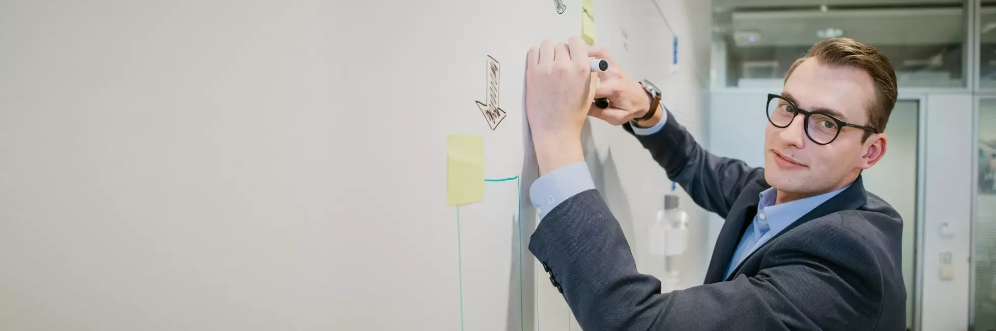 Mr von Podewils, Dürr Consulting supports taking production efficiency to the next level in factory planning. He draws scenarios on the whiteboard
